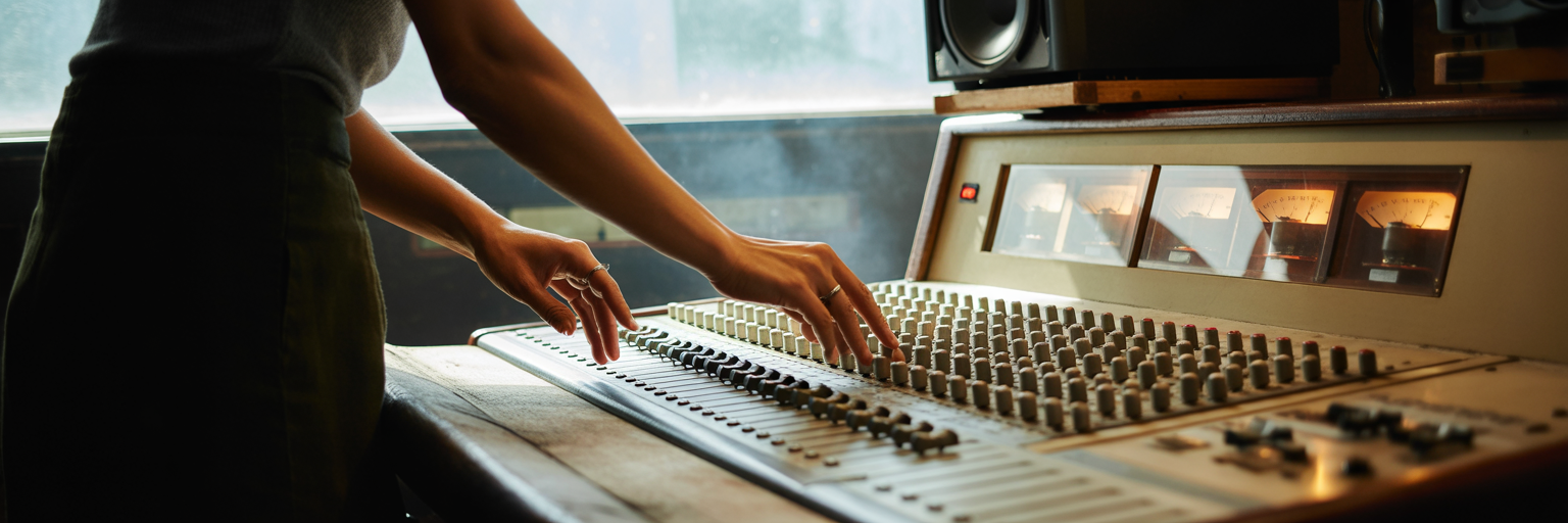 Hands adjusting faders on a sound mixing console.